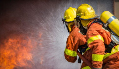 2 firefighters in full gear fighting a fire.