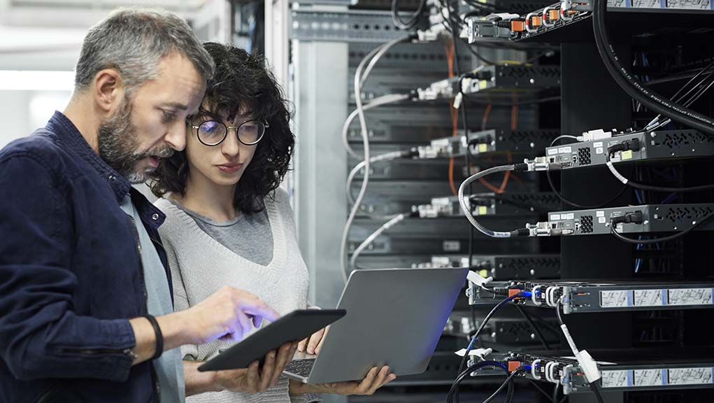 Male technician showing digital tablet to female coworker. Engineer working with colleague at workplace. They are in server room.