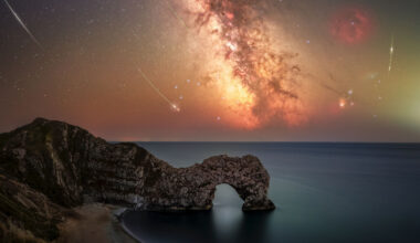 Perseid meteors are pictured alongside the Milky Way above a coastal scene featuring an arch-like rocky outcrop