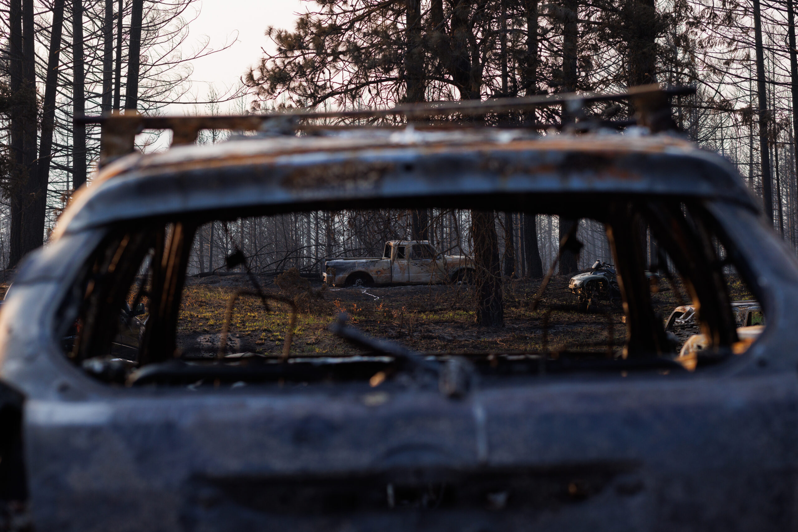 A view through the burst out rear window of a charred car in the Little Shuswap community east of Kamloops. Through the broken rear window and windshield, another charred truck sits among the trees in the disastrous remains of the Bush Creek East fire.