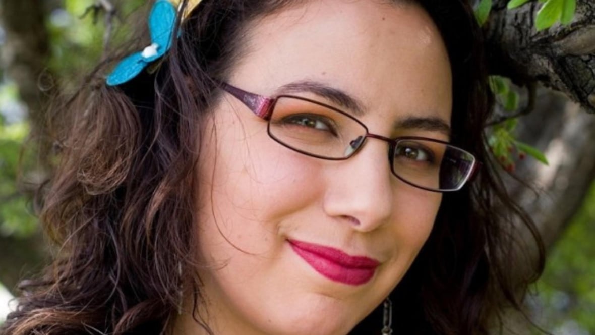 A woman wearing glasses and a blue flower in her hair is smiling at the camera. 