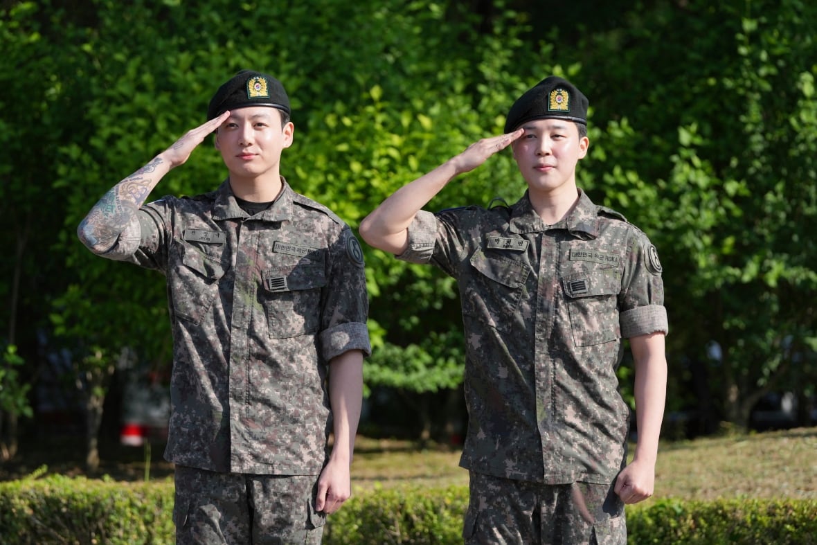 Two Korean men in military uniforms saluting outside on a sunny day. 