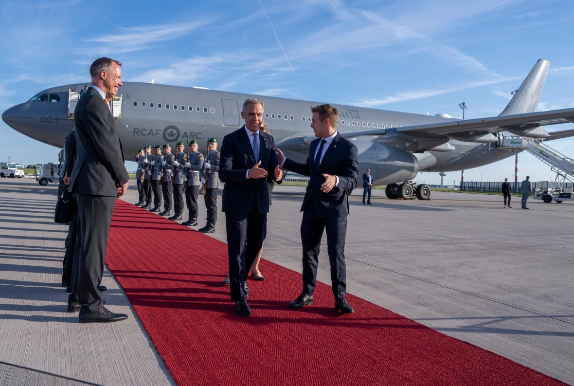 A man walks down a red carpet leading from an aircraft with others lined up around him.