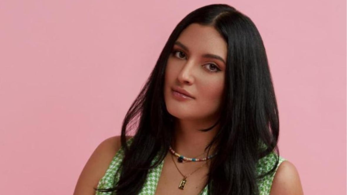 A woman with long dark hair against a pink background.