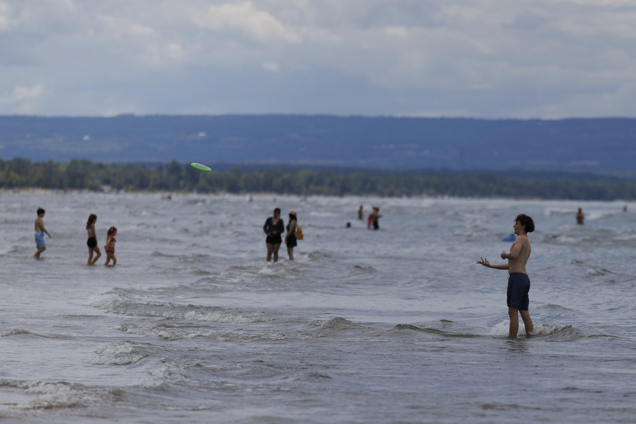 Shin-deep in the waves at Wasaga Beach, a person throws a Frisbee.
