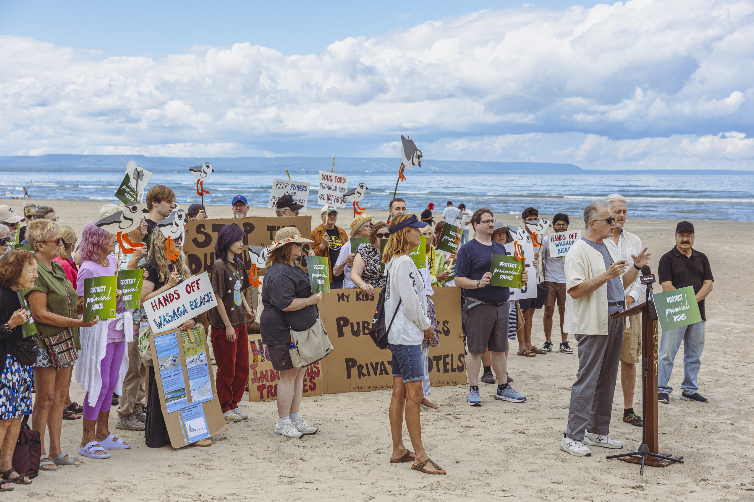 A few dozen protesters gather on Wasaga Beach to voice their opposition to the Ford government's proposal to transfer parts of Wasaga Beach Provincial Park to the Town of Wasaga Beach. Many hold signs that say: "Protect Provincial Parks."