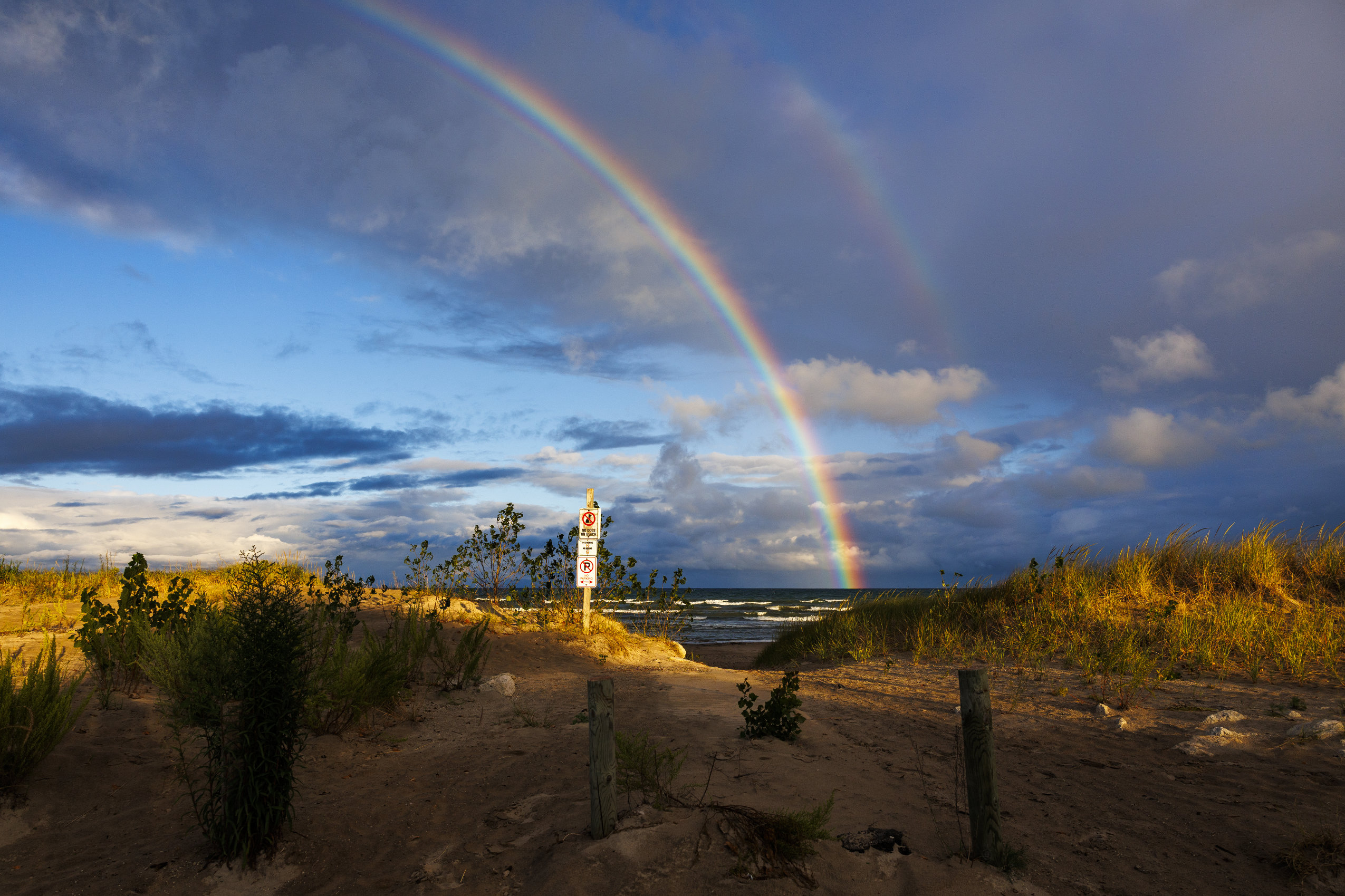 A double rainbow stretches across the sky amid dramatic sunrise lighting on Wasaga Beach.