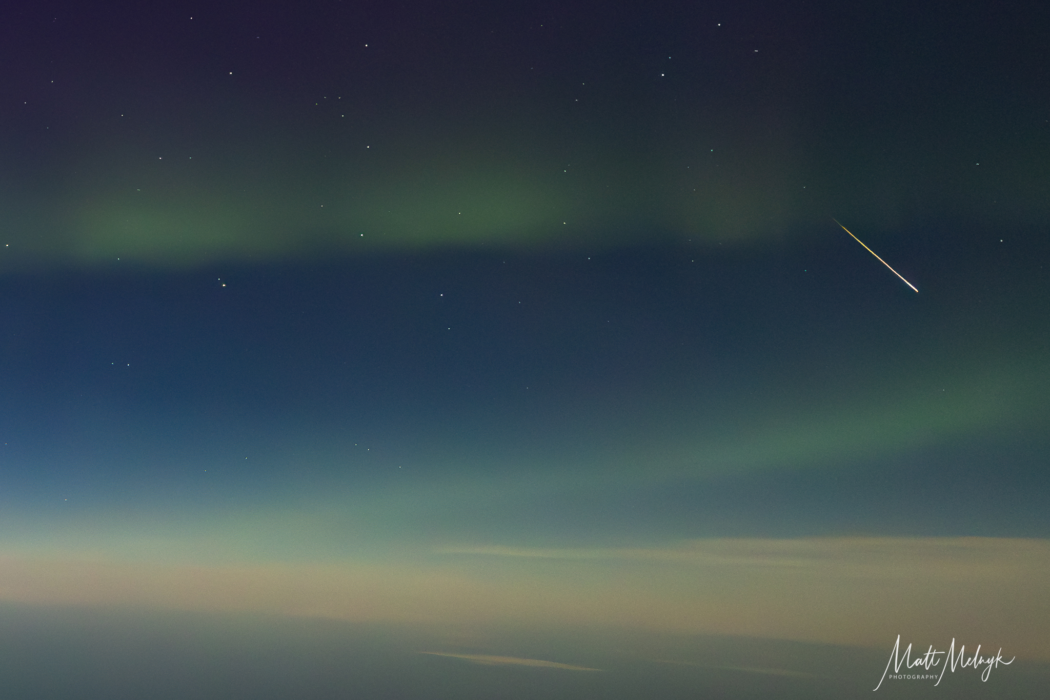 A lone meteor is pictured streaking through a sky wreathed in a twisting green aurora in a scene shot from an airplane. The curvature of Earth is visible below.