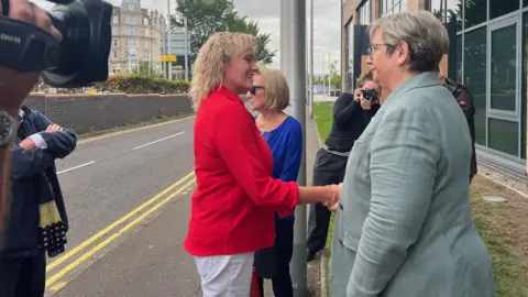 Sandie Peggie - a woman in a red jacket and with shoulder length blond hair - shakes hands with Joanna Cherry, a woman with short blonde hair and a grey suit.