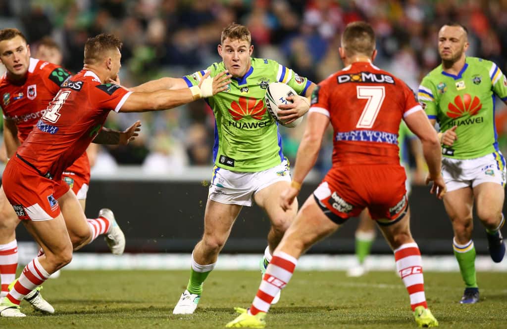 A rugby league player in a lime-green jumper holds the ball as he runs towards other players in red uniforms