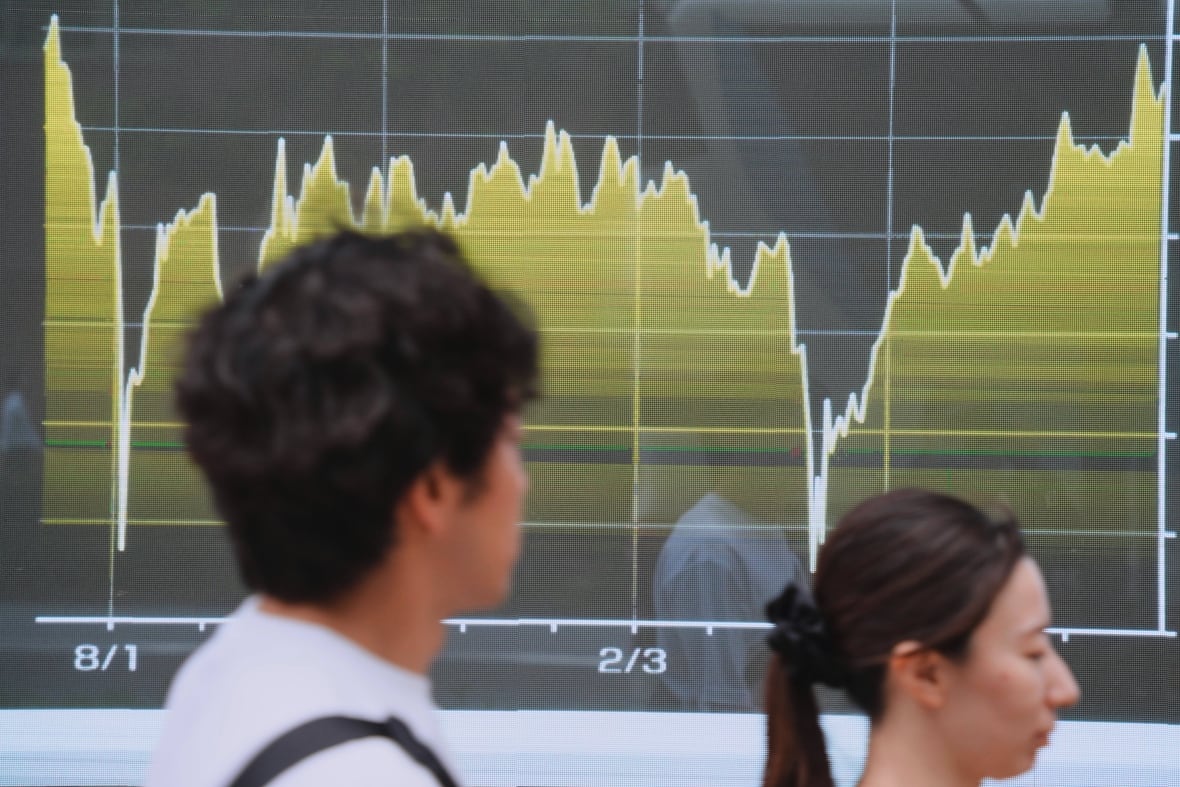 Two people walk past a graph that shows a line going up and down. 