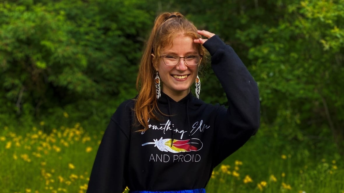 A young woman with red hair and glasses is smiling at the camera. 