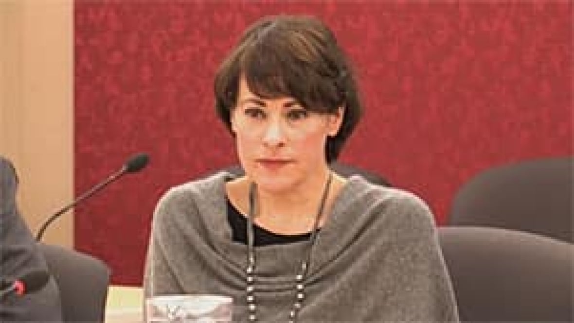 A woman with short hair speaks in a red chamber.