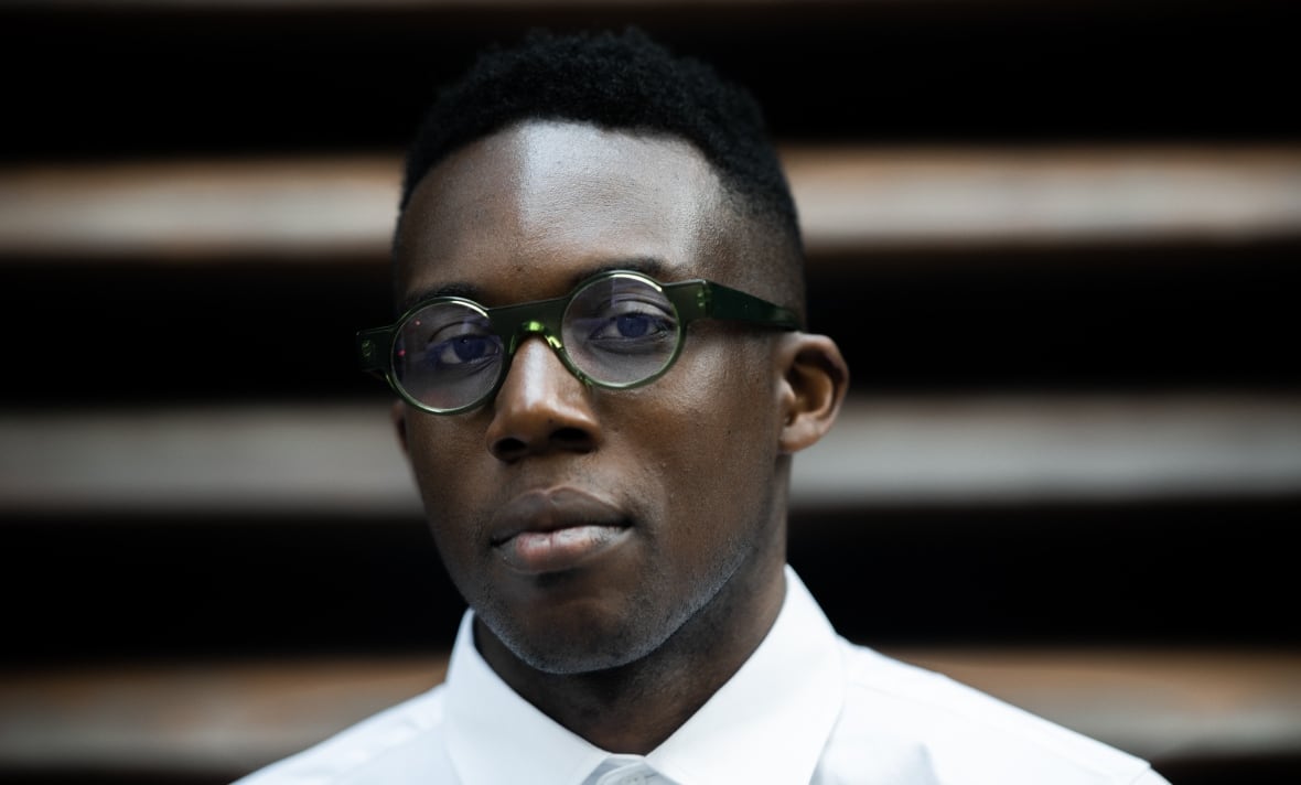 A Black man wearing a white dress shirt is smiling at the camera. 