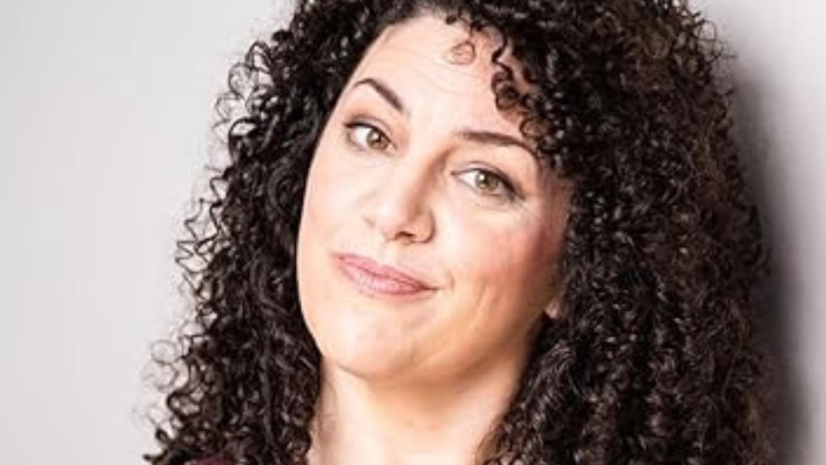 A woman with long dark curly hair is smiling at the camera. 