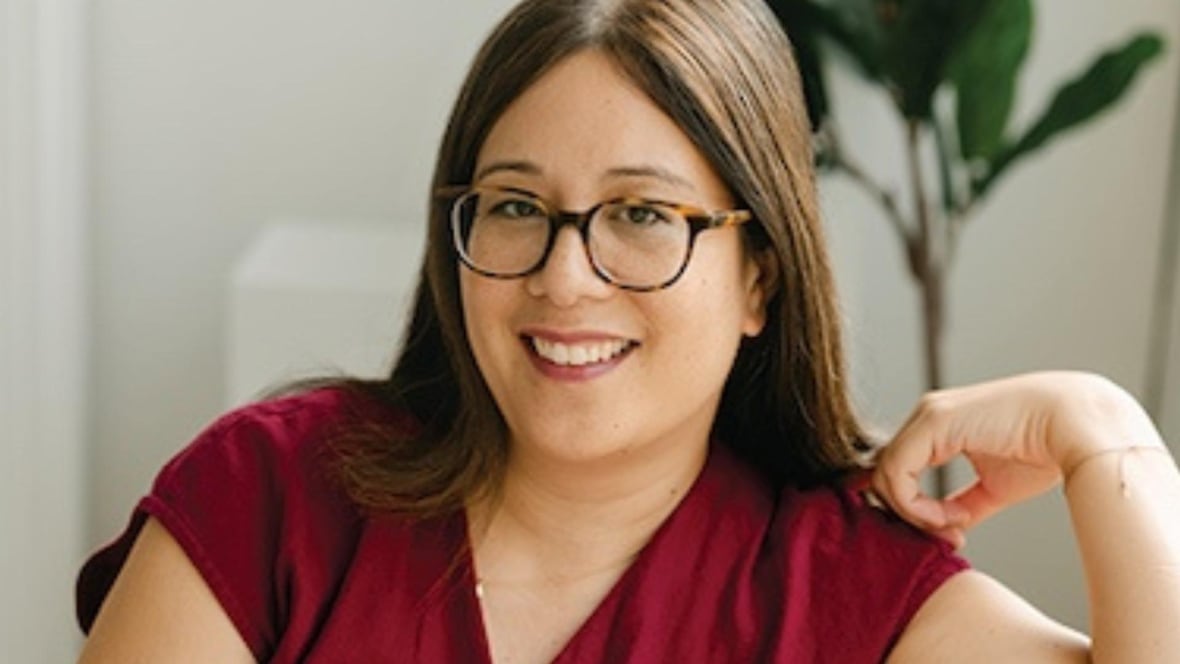 A woman wearing black framed glasses is smiling at the camera. 