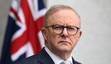 Anthony Albanese, in a suit, is standing in front of an Australian flag.