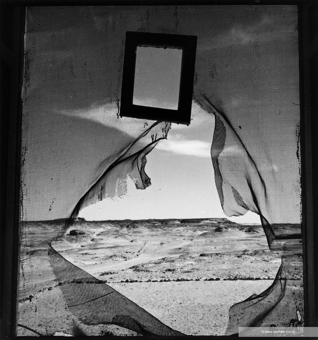 Black and white photo of a torn screen revealing a desert landscape.