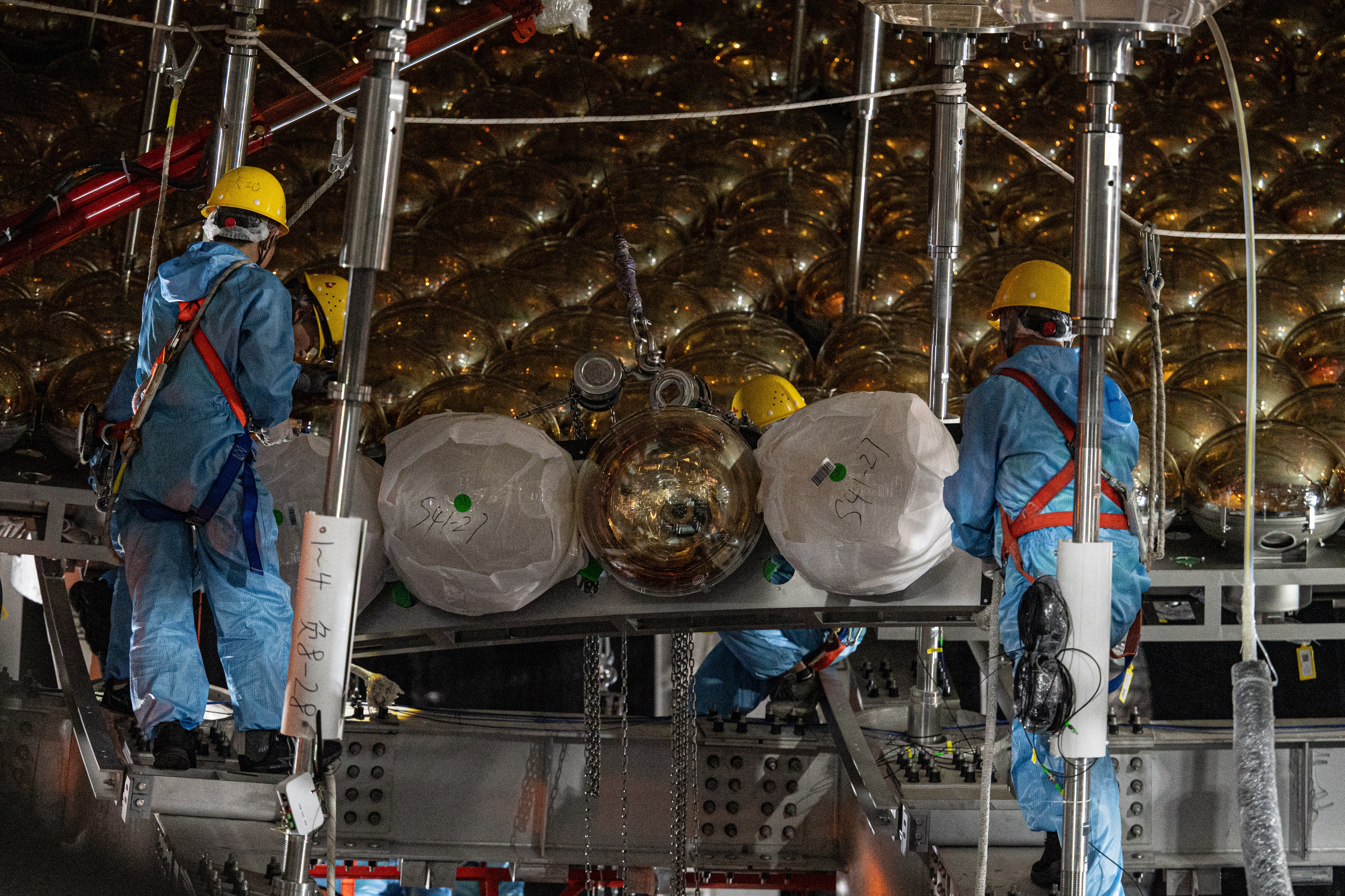 Workers installing photomultiplier tubes onto a neutrino detector at the Jiangmen Underground Neutrino Observatory (JUNO).