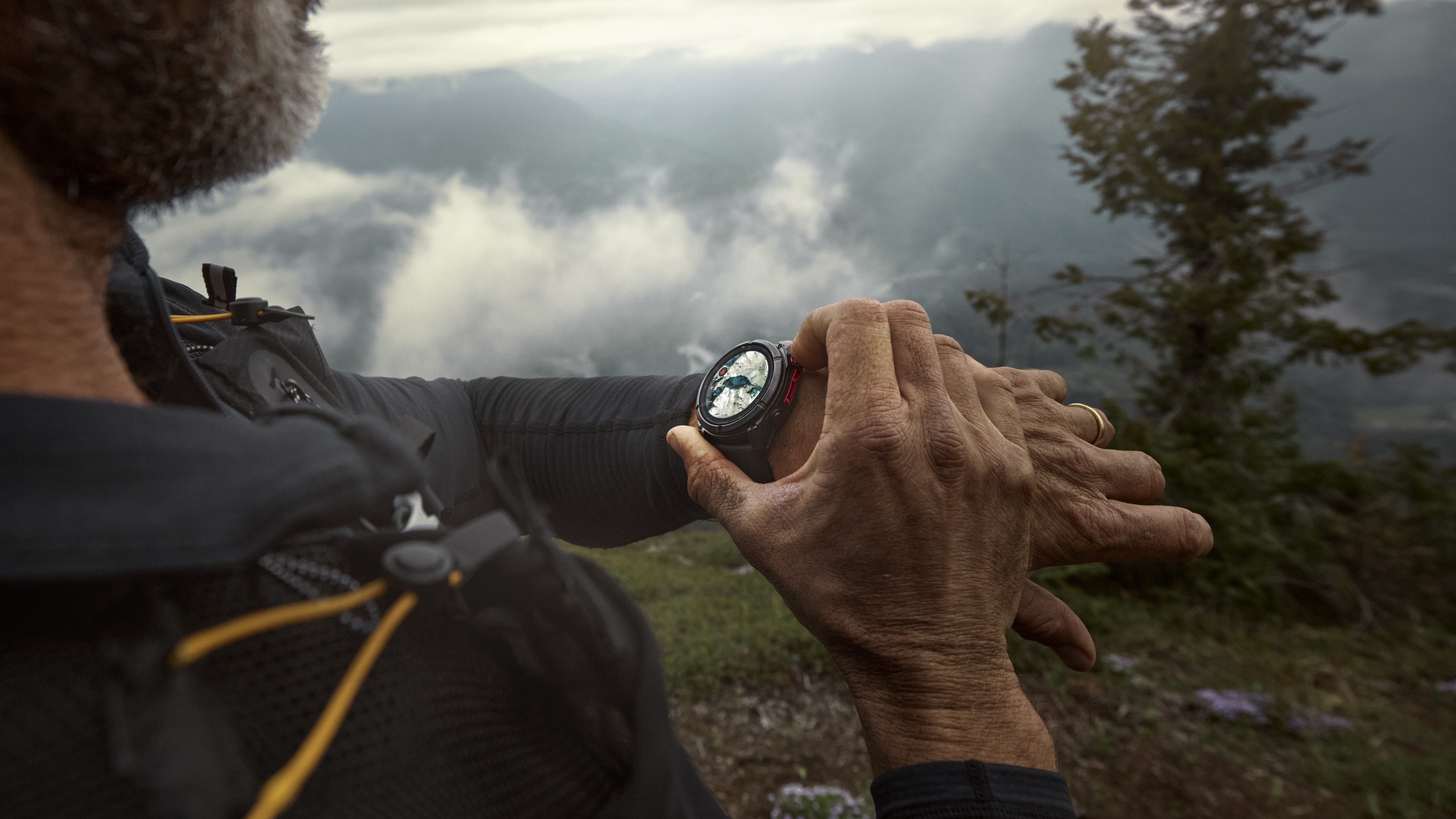 A photo of a man in the mountains wearing a Garmin Fenix 8 Pro, using it to check his nearby mapped location.