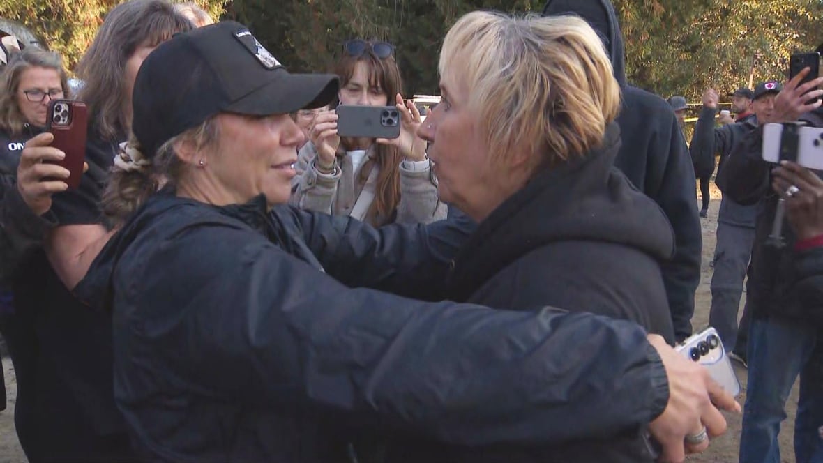 Two women embrace as others in the crowd capture the moment in their cell phones.