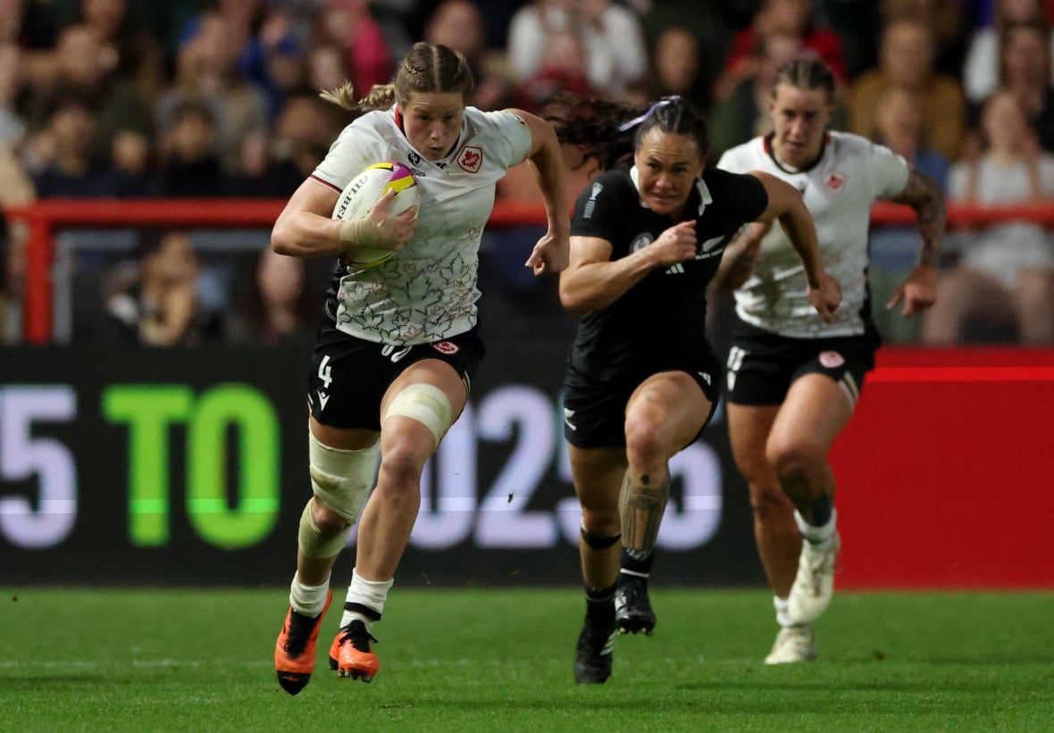 A rugby player chasing a rival player whose teammate is behind them during a match, with spectators watching.