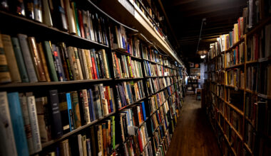 A narrow aisle lined with tall bookshelves filled with books in a dimly lit bookstore.