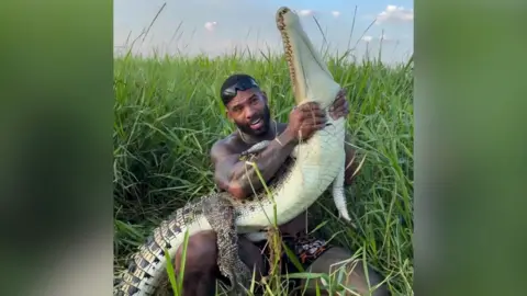 Instagram Mike Holston is seen holding a juvenile saltwater croc around the neck in grassland