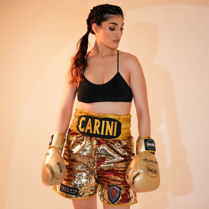 Female boxer wearing golden boxing gloves and sequin shorts, standing confident while reflecting on harassment that affected her career. Female boxer wearing golden boxing gloves and sequin shorts, standing confident while reflecting on harassment that affected her career.