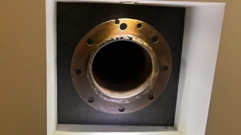 Brass valve in a black square mounted in a recess on a wall