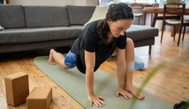 Woman stretches her hips in front of a couch with two yoga blocks to the side of her