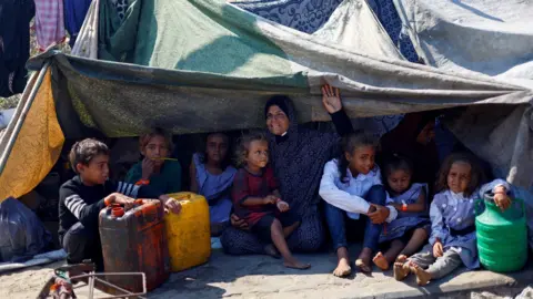 Reuters Displaced Palestinians from northern Gaza sit beneath a makeshift shelter on a roadside in central Gaza (18 September 2025)