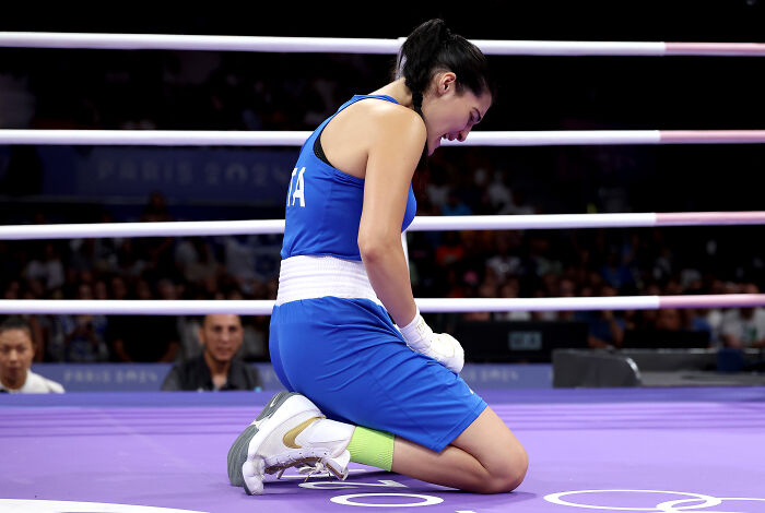 Female boxer kneeling in the ring, wearing blue gear, representing the boxer who refused to fight Imane Khelif amid harassment claims. Female boxer kneeling in the ring, wearing blue gear, representing the boxer who refused to fight Imane Khelif amid harassment claims.