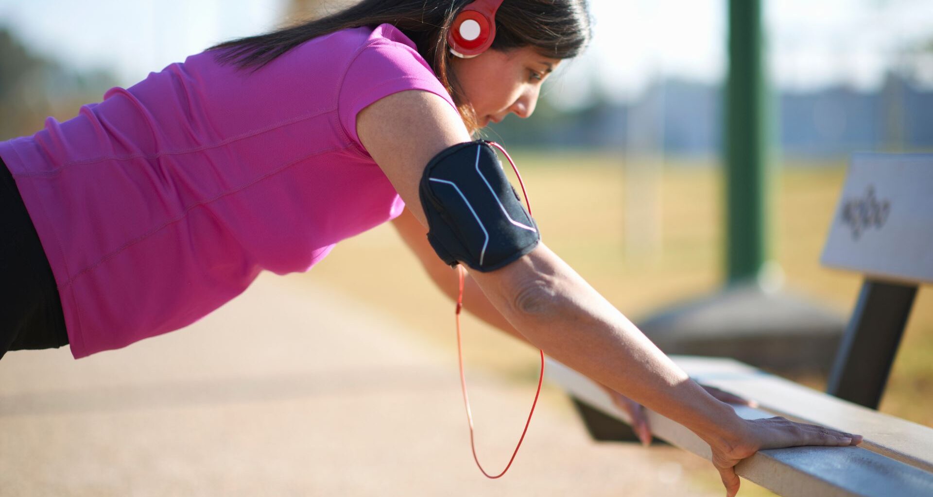 Woman wearing headphones and activewear, doing press up on a bench, highlighting the benefits of 1 minute of exercise per day