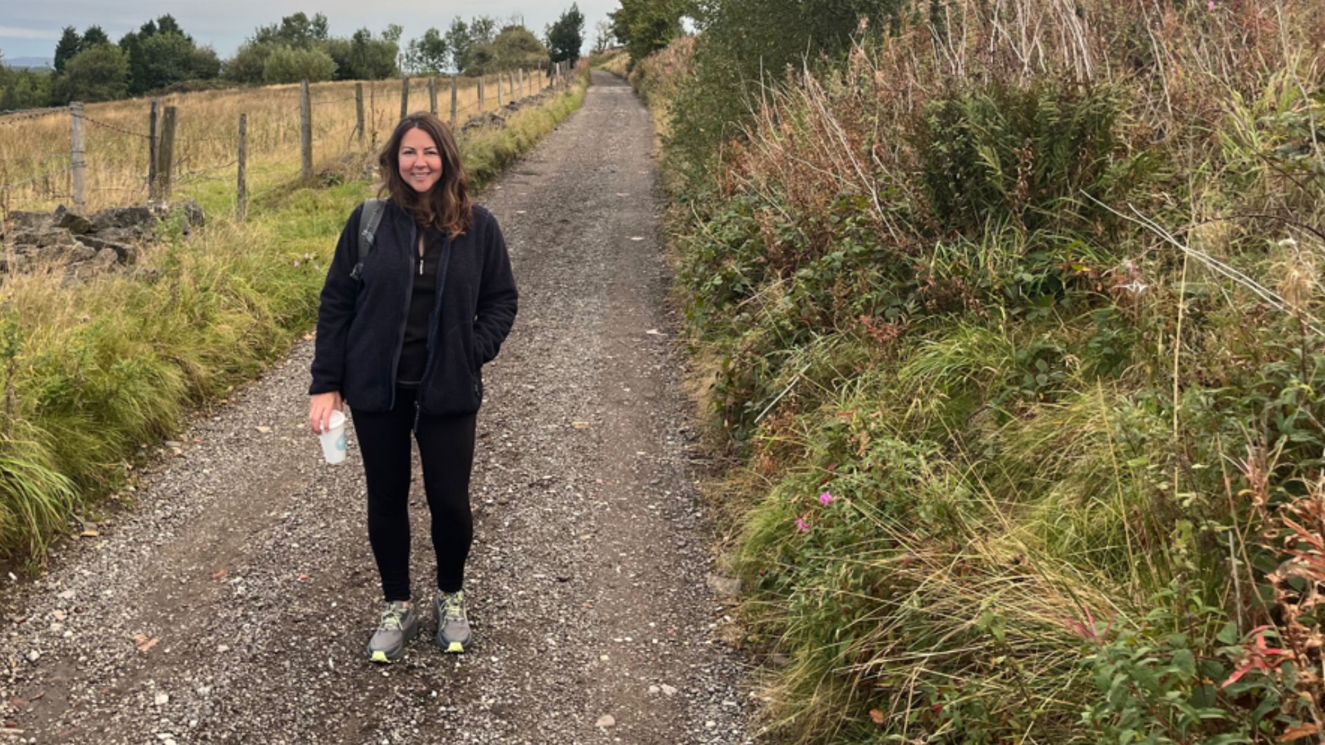 Susan Griffin doing the 6-6-6 walking workout through path in field, smiling at camera