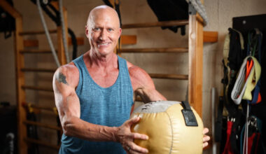 Man in gym smiling at camera holding medicine ball