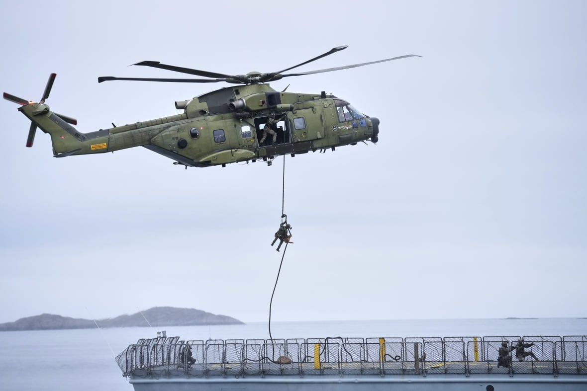 A helicopter hovers over ship with one person rapelling during in a military exercise over a bod