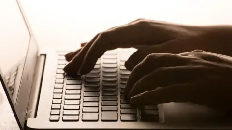 Dominic Lipinski/PA Wire Hands typing on a laptop keyboard.