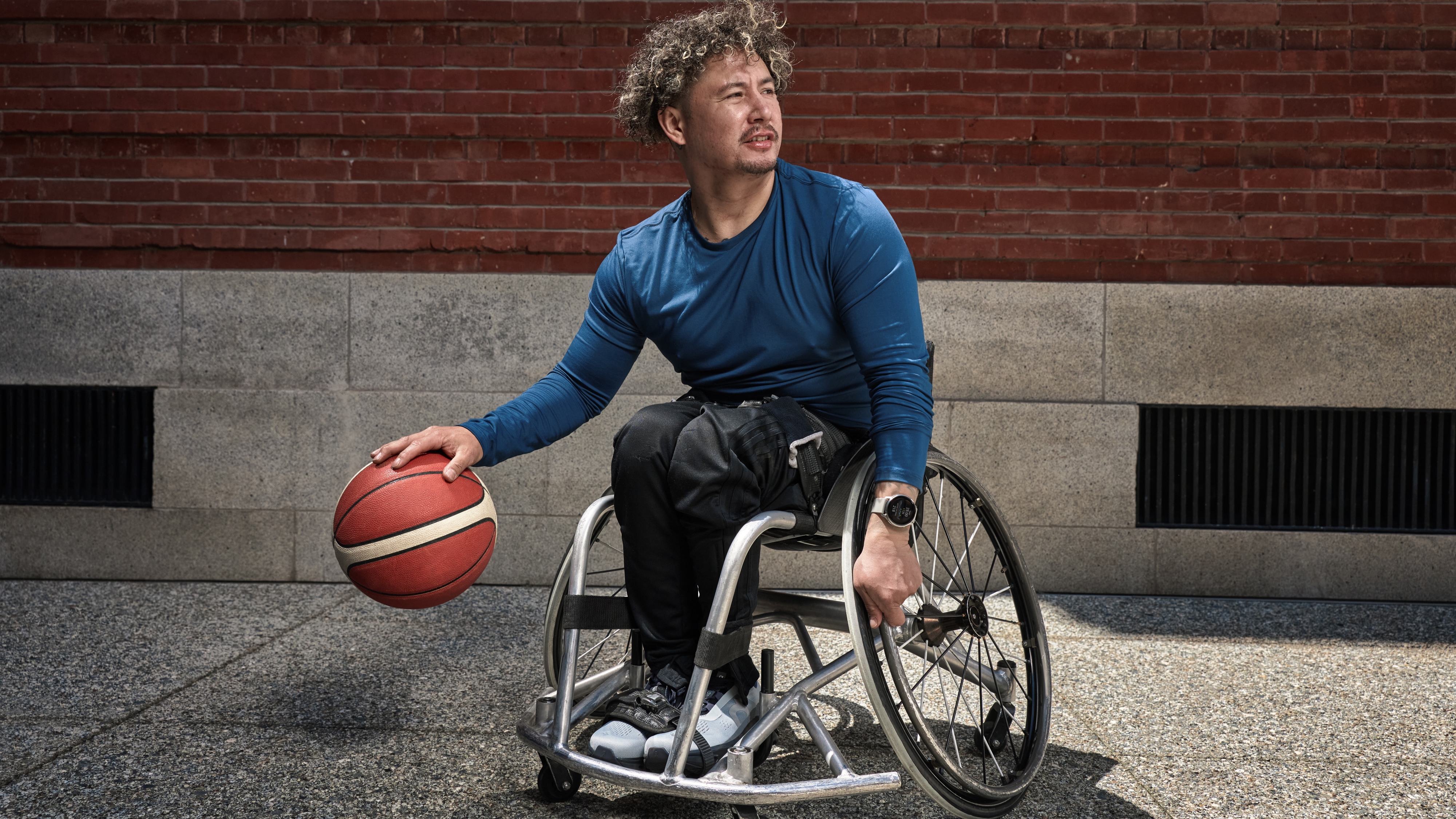 A photo of a disabled basketball player in a wheelchair, bouncing the ball while wearing the Garmin Venu 4 in the other.