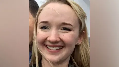 Andrea Brady A close-up photo of Jessica Brady who is smiling broadly and looking directly at the camera, with long blonde hair, brown eyes and a visible earing in her left ear.