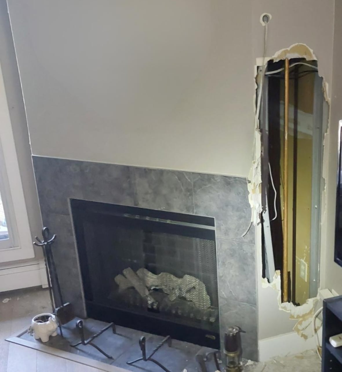 A large hole is knocked out in the wall next to a fireplace. 