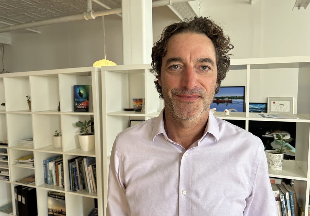 A man poses for a photo inside an office with bookshelves in the background.