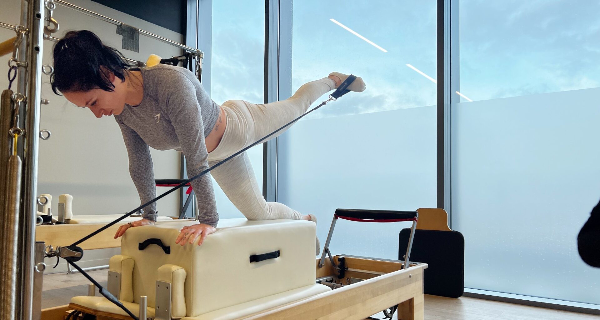 Writer Sam on a reformer Pilates bed on hands and one knee extending her left leg behind her, front view