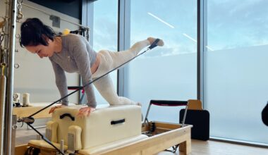 Writer Sam on a reformer Pilates bed on hands and one knee extending her left leg behind her, front view