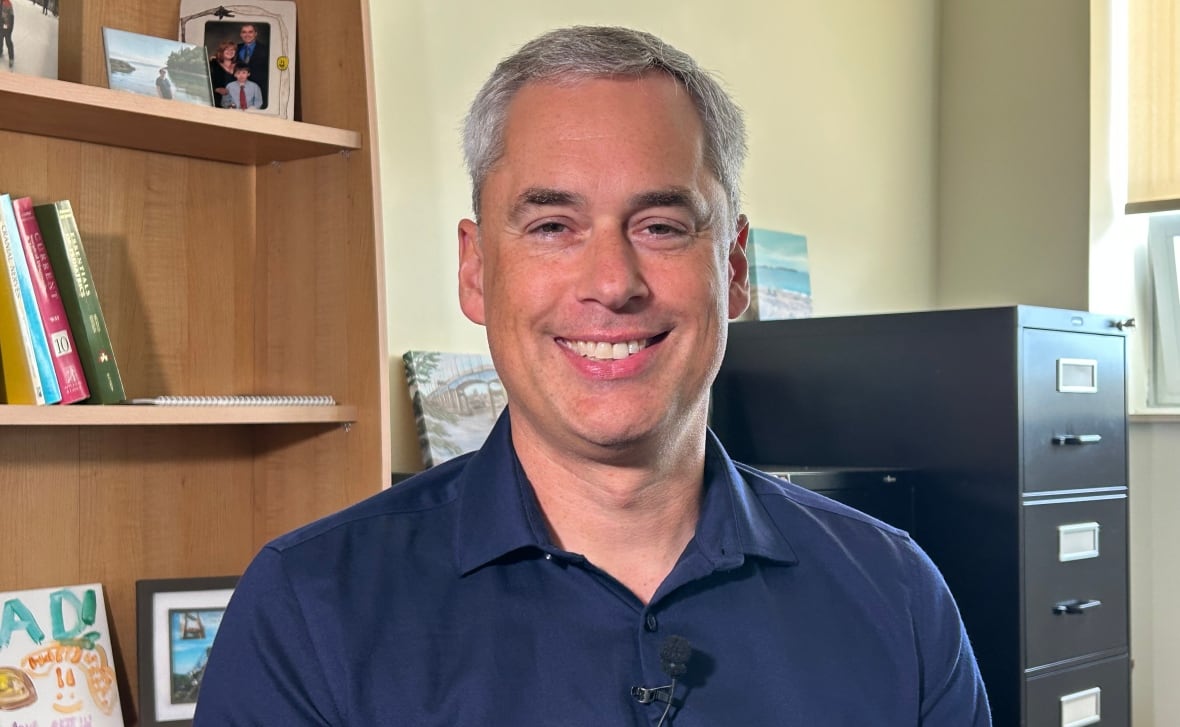A white man with grey hair, wearing a blue shirt.
