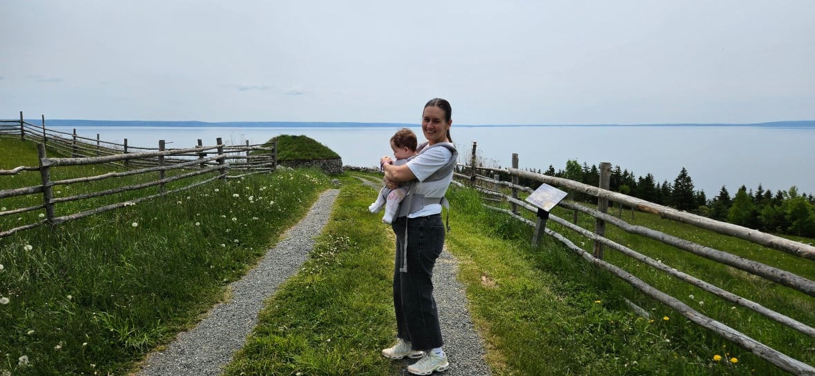 A woman holding a baby overlooks the ocean.
