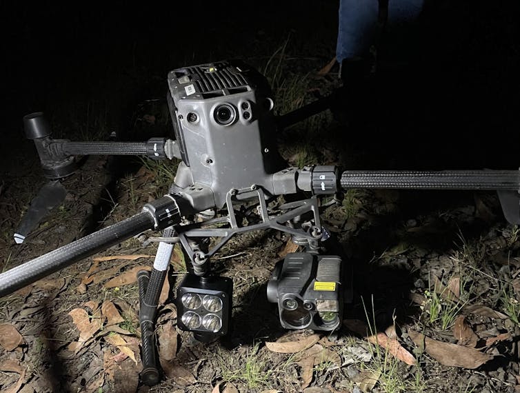 A grey drone with a light and a camera attached on the ground.