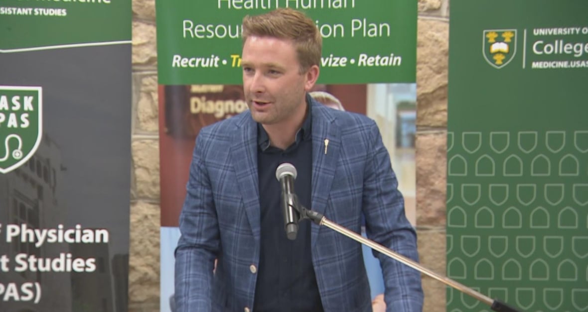 A blonde man in a suit speaks at a podium.