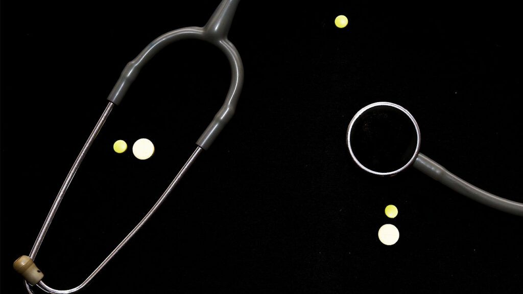 A stethoscope used to listen to the heart and a few beta blocker pills on a flat dark surface