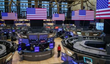 A woman walks on the trading floor of the New York Stock Exchange, surrounded by trading stations and large digital American flags.